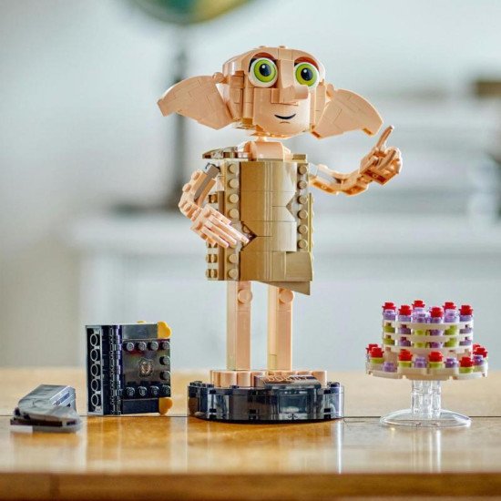 LEGO figurka Dobbyho stojí na podstavci se jmenovkou, drží Harryho ponožku v deníku Toma Riddla a vedle něj levituje pudinkový koláč tety Petunie.