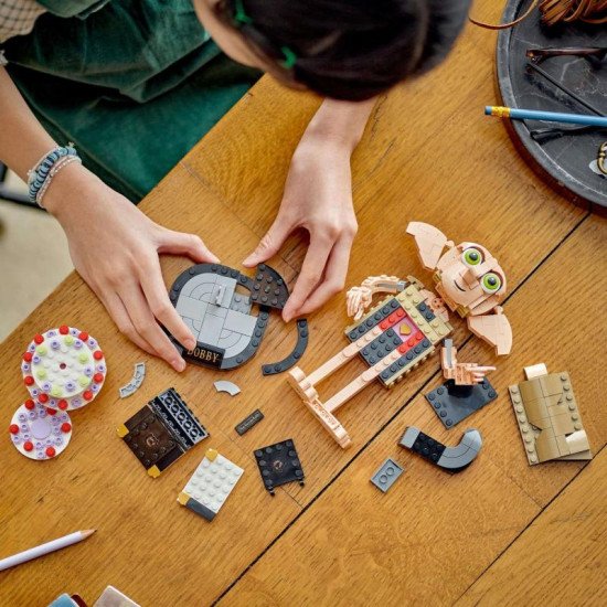 LEGO figurka Dobbyho stojí na podstavci se jmenovkou, drží Harryho ponožku v deníku Toma Riddla a vedle něj levituje pudinkový koláč tety Petunie.
