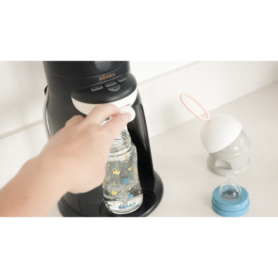Přístroj na přípravu umělého mléka s funkcí ohřívání láhve s nápojem nebo sklenice s příkrmem.