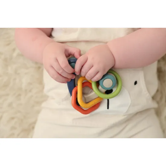 Barevné chrastítko ve tvaru trojúhelníku se třemi přívěsky různých tvarů.