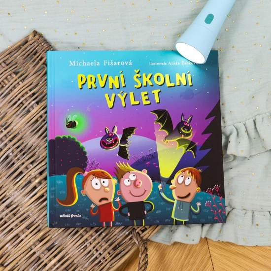 Skupina prvňáků s batohy na zádech stojí na lesní cestě, smějí se a ukazují si na mapě cestu k tábořišti.